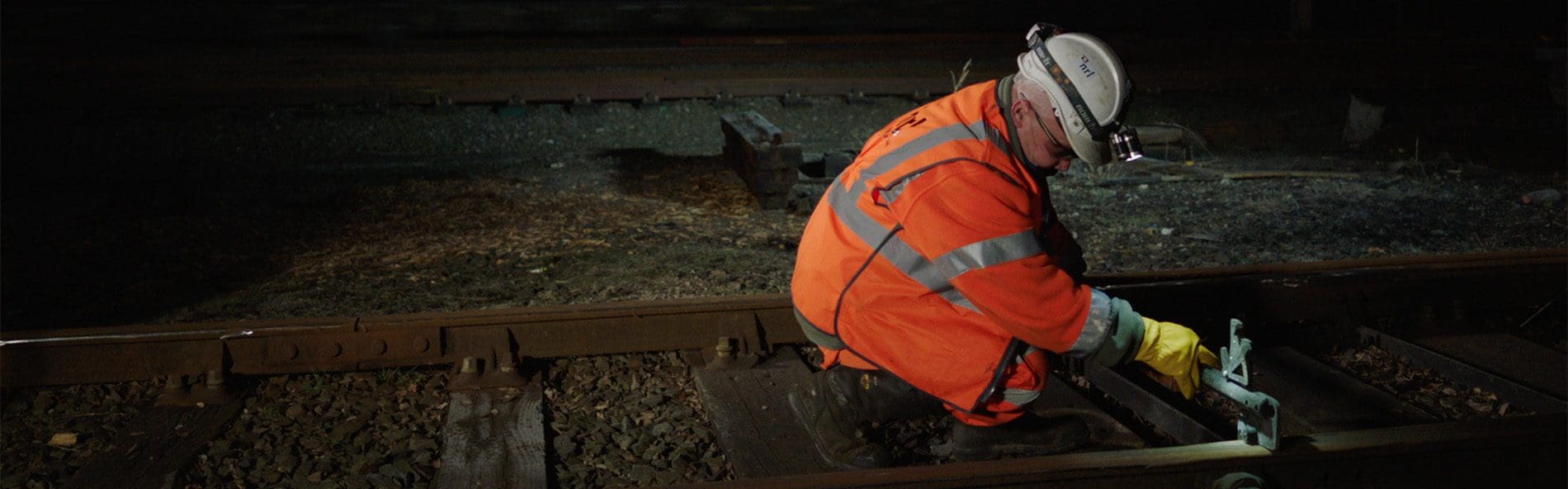 An NRL Rail contractor crouched down doing track maintenance, wearing full PPE