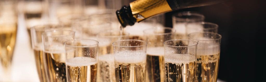 a close up of lots of full champagne glasses with a bottle being poured