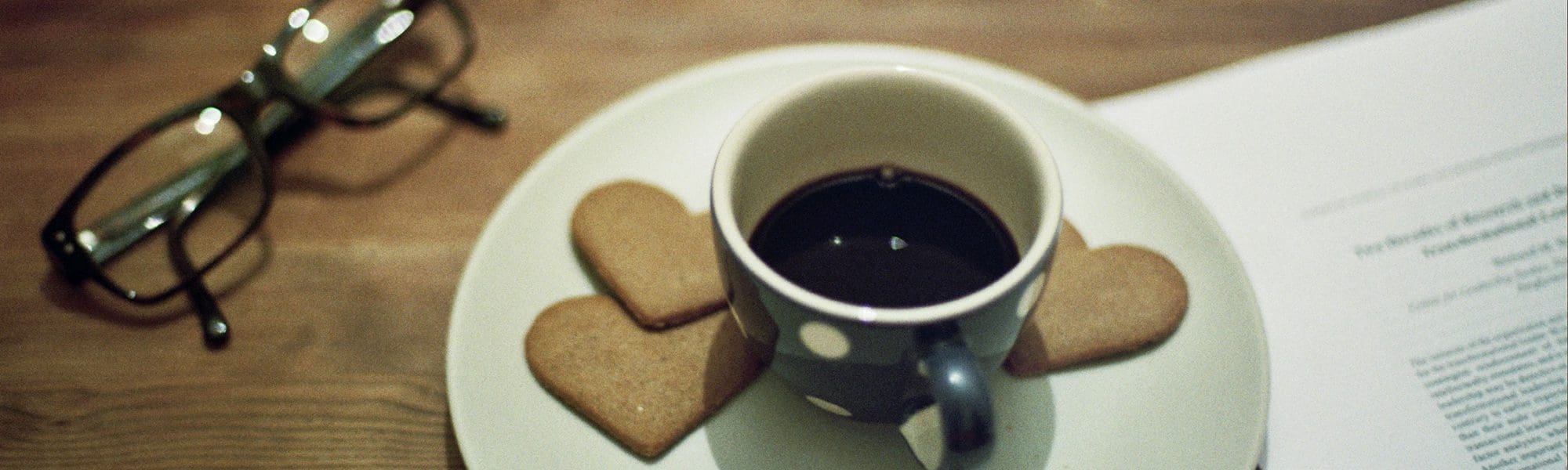 a picture of a cup of black coffee on a plate with 3 heart shaped biscuits