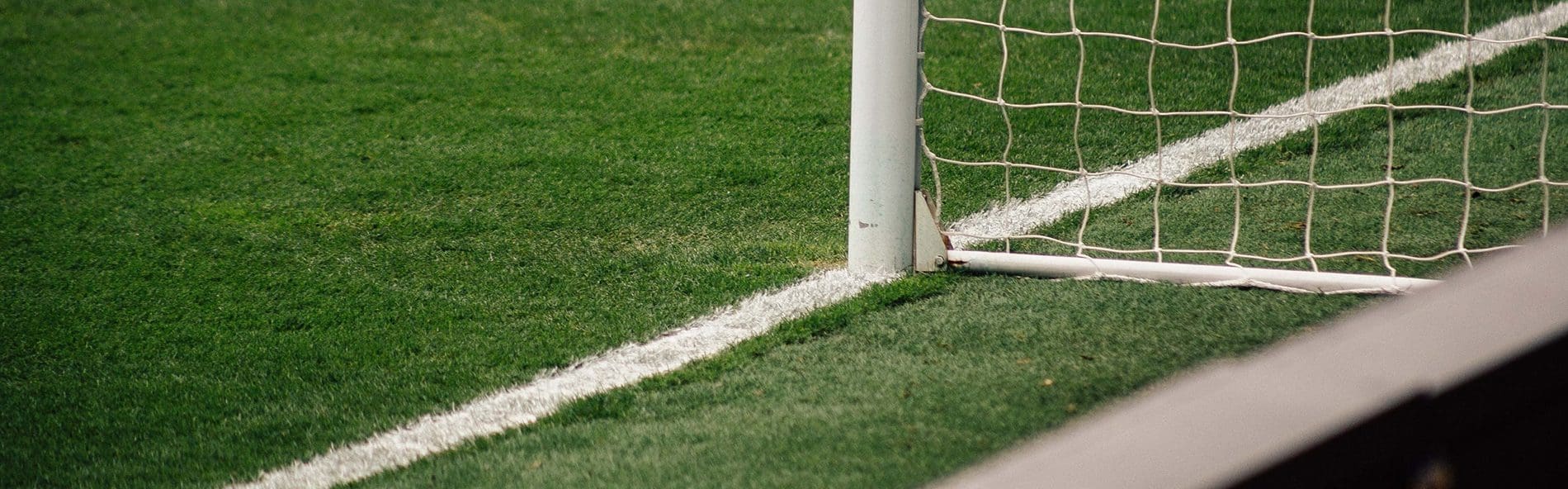 a close up of the bottom of a football goal post and net, pitch in the forefront