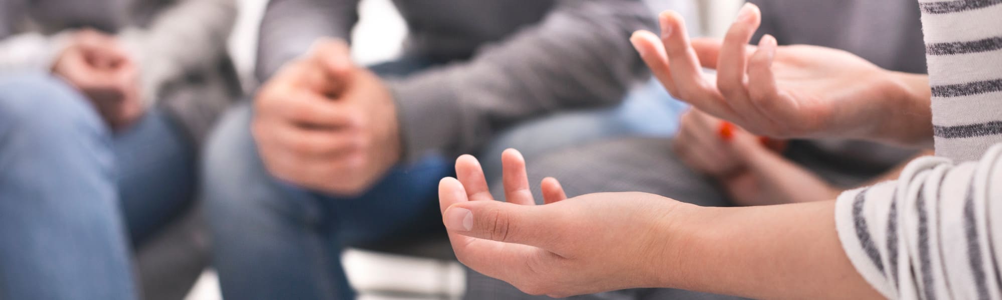 Group counselling session, focus on a woman's open hands resting on her lap, with only arms and hands visible.