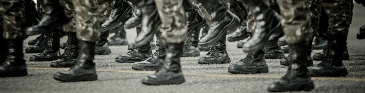 Close-up of a row of soldiers in camo uniforms and black boots, showing only their legs.