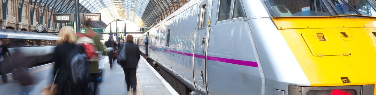 People at a railway station with a yellow and silver train stopped at the platform.