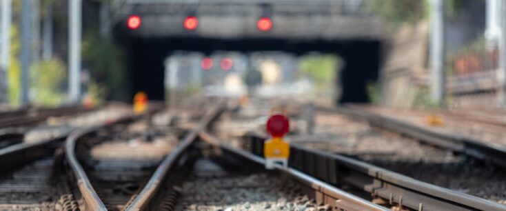 Blurred railway tracks with red light signals visible in the background.