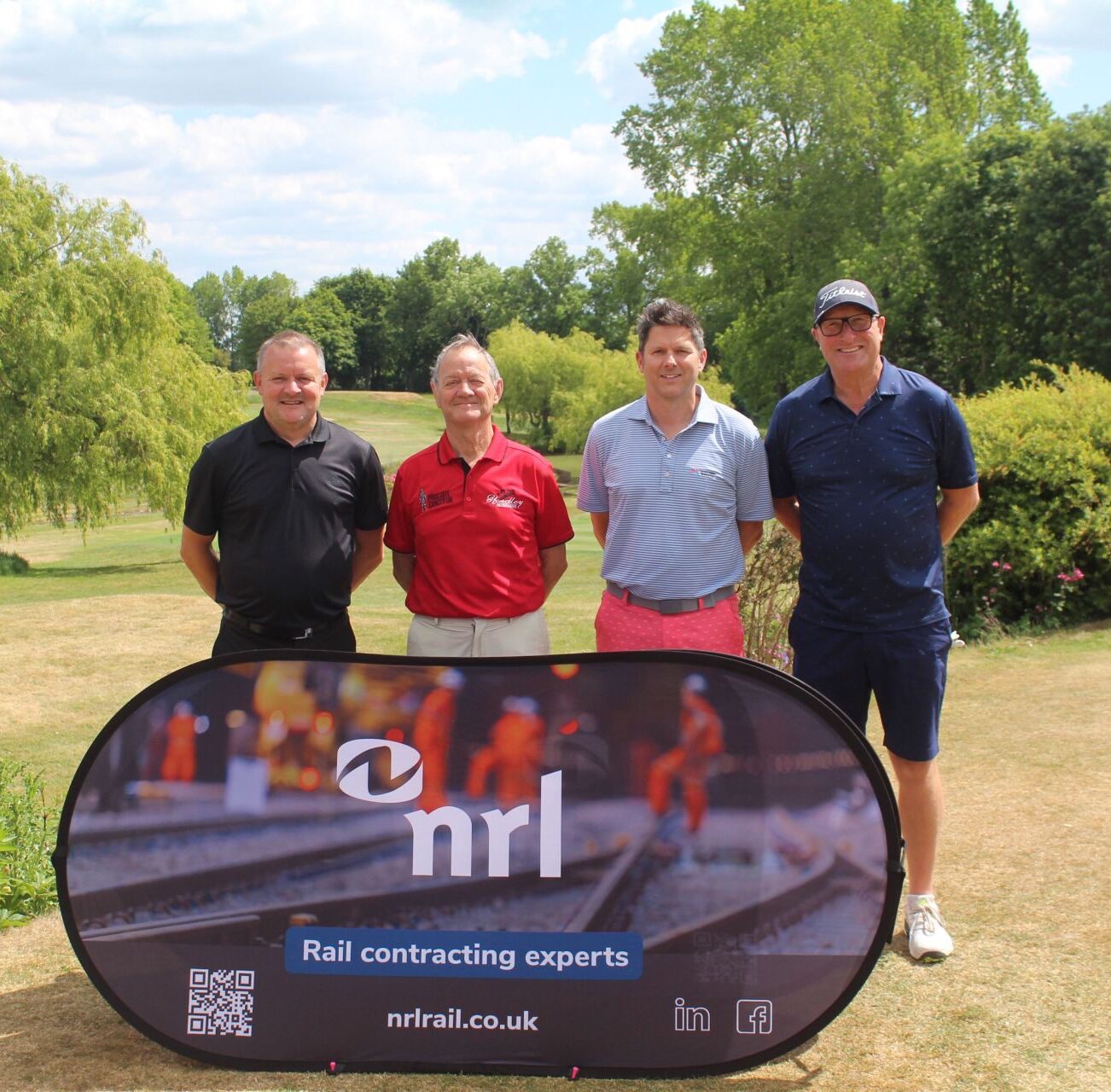 Four men behind an NRL Rail banner at Rail Golf Day 2025, blue sky and trees in the background.