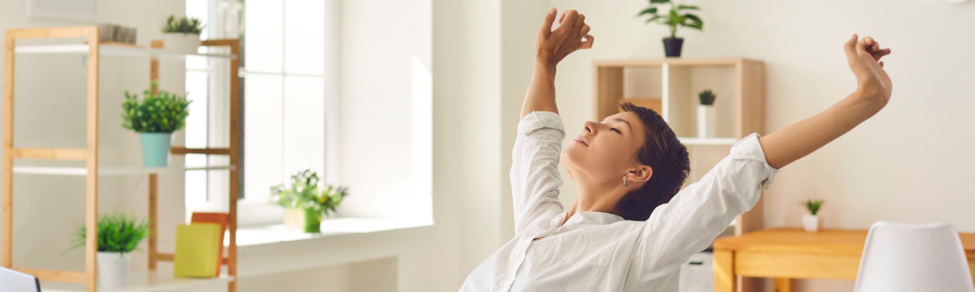 A lady stretching her arms over her head and leaning back on a chair, closing her eyes.