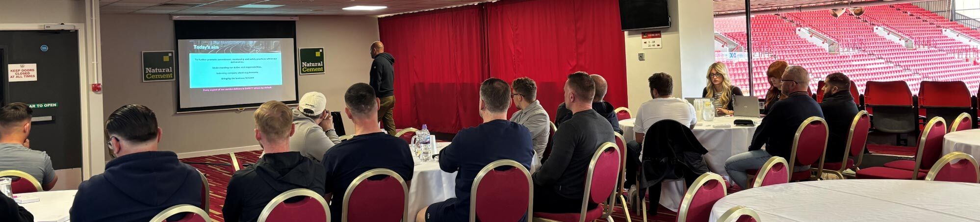 Rail Contractors sat in a conference room, all looking at the presentations screen, Brett Hawke speaking at the front.