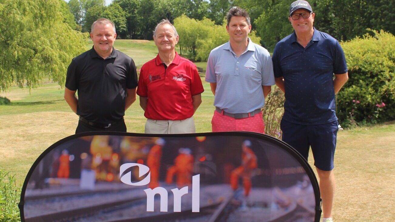 Four people stand behind an NRL branded banner on a grassy outdoor area with trees behind.