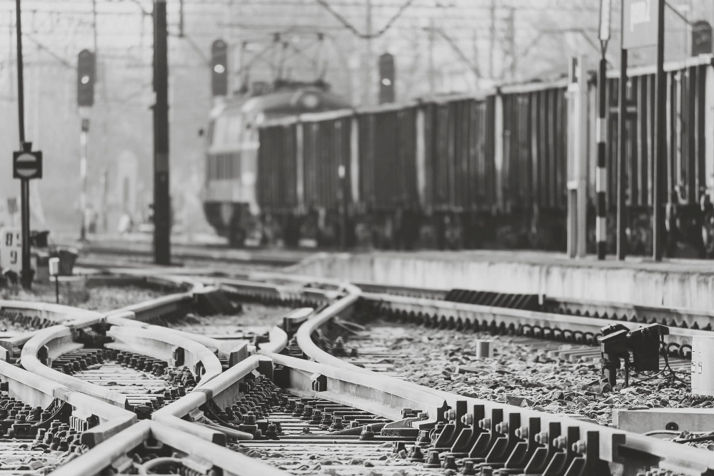 Multiple railway tracks split and cross in the foreground while a freight train passes in the background.