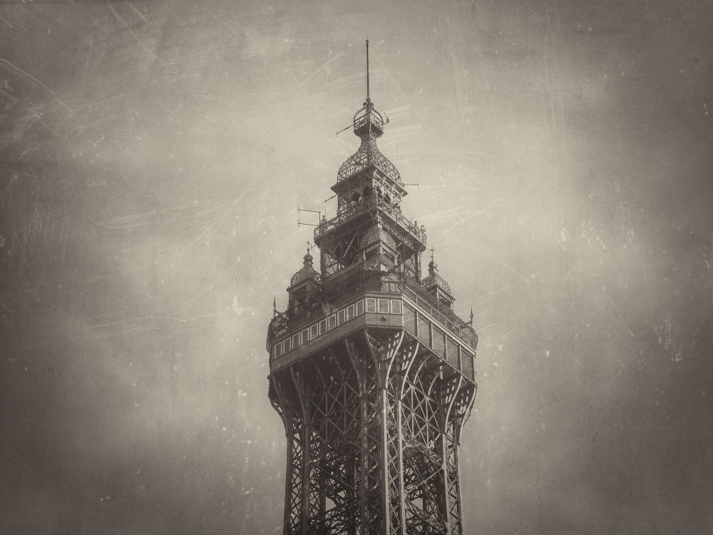 Tall lattice tower rises against a cloudy sky, showing detailed metal framework and observation level.