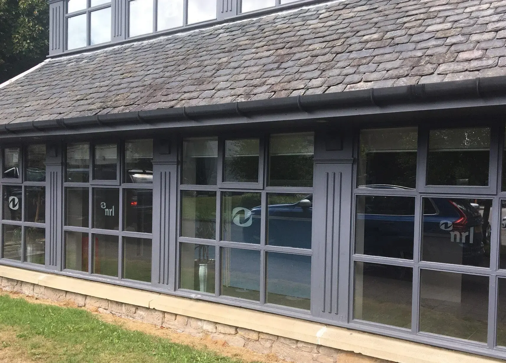 Office building with grey framed windows and visible NRL logos on glass panels above a grassy area.