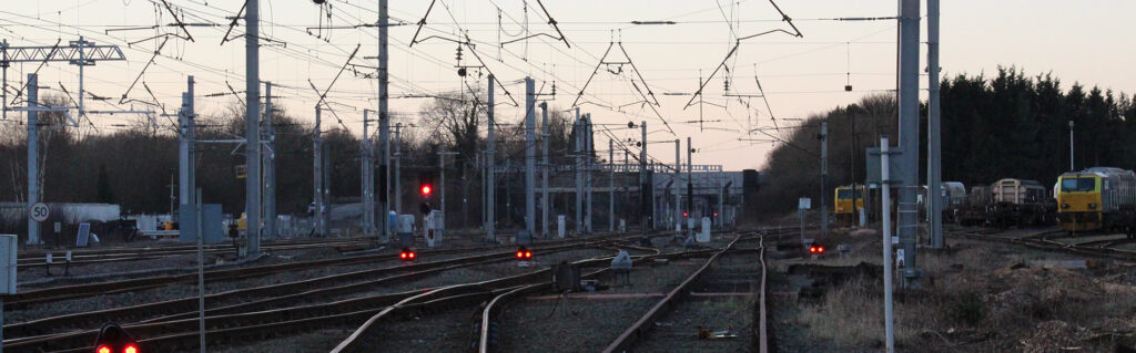 Multiple railway tracks with red signal lights and overhead cables leading towards a station.
