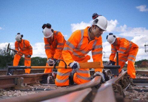 Four workers in high-visibility clothing kneel on railway track using tools to carry out maintenance work.