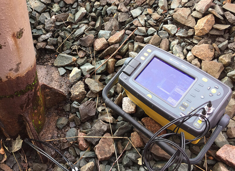 Portable testing device connected by cables to a rail, used for ultrasonic inspection on track.