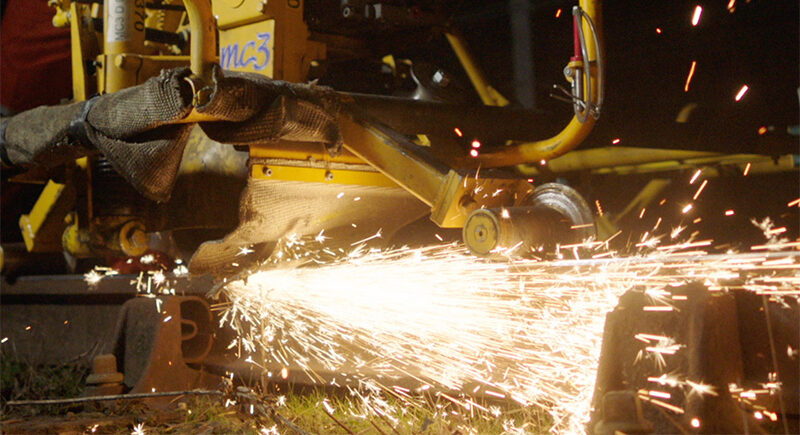 Grinding equipment moves along a rail, producing bright sparks during track maintenance.