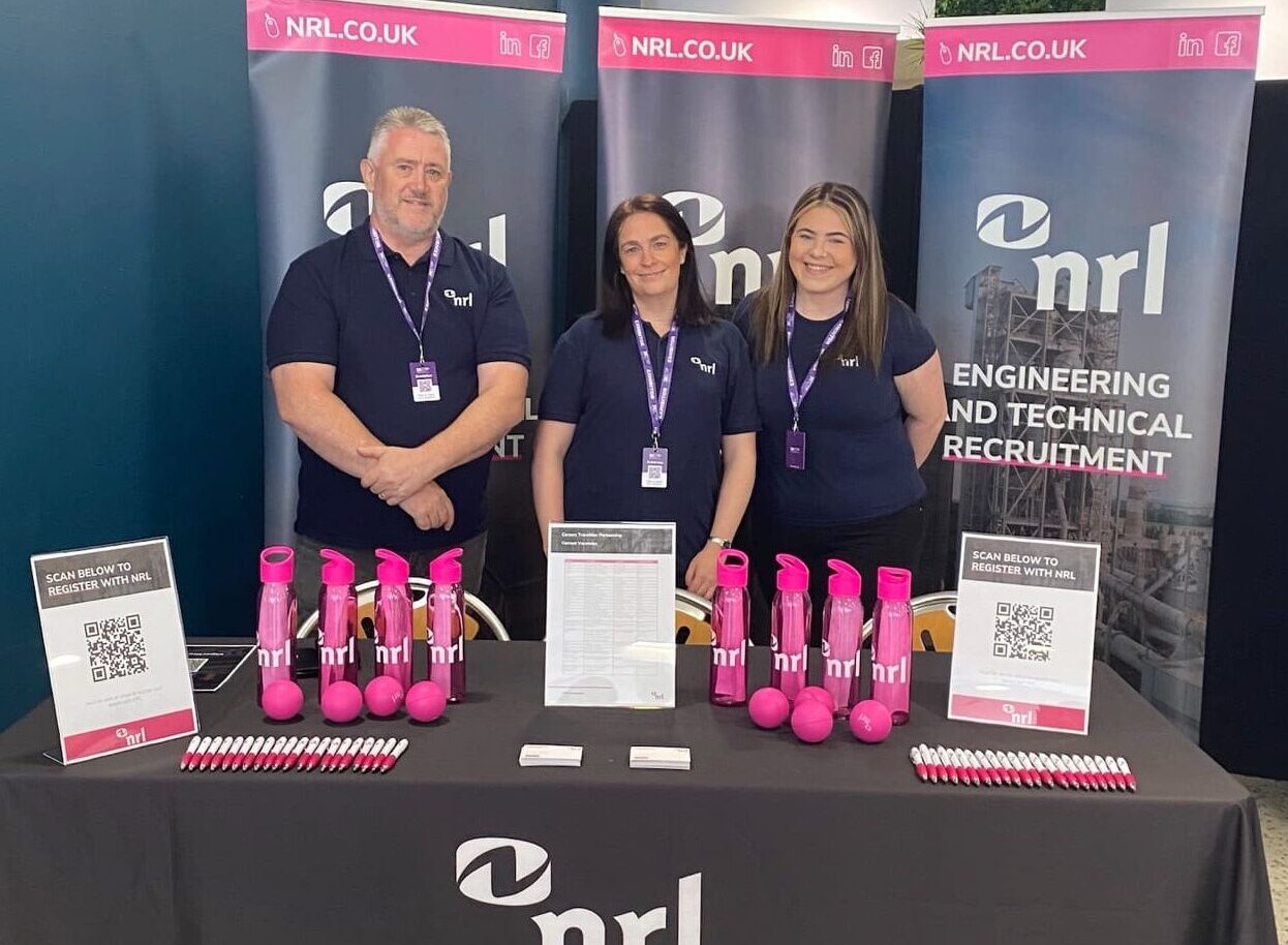 Three people stand behind an NRL branded stand displaying pink bottles, leaflets and QR code