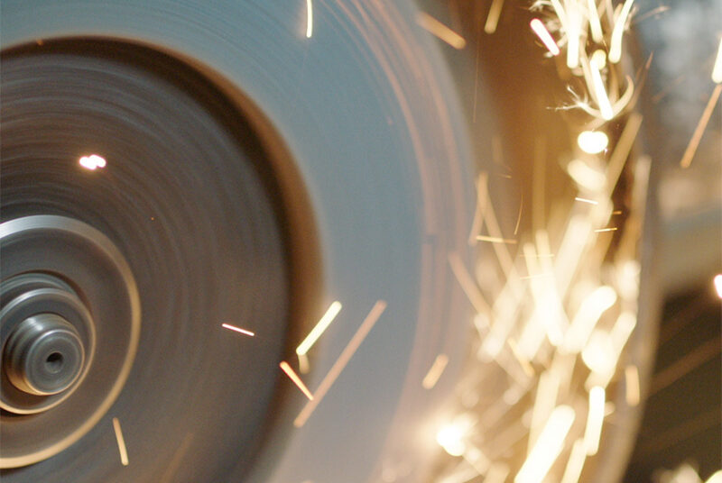 Close-up of a spinning grinding wheel producing sparks while cutting metal.