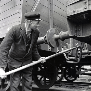 Worker uses a long lever to connect coupling between freight wagons on a railway track.