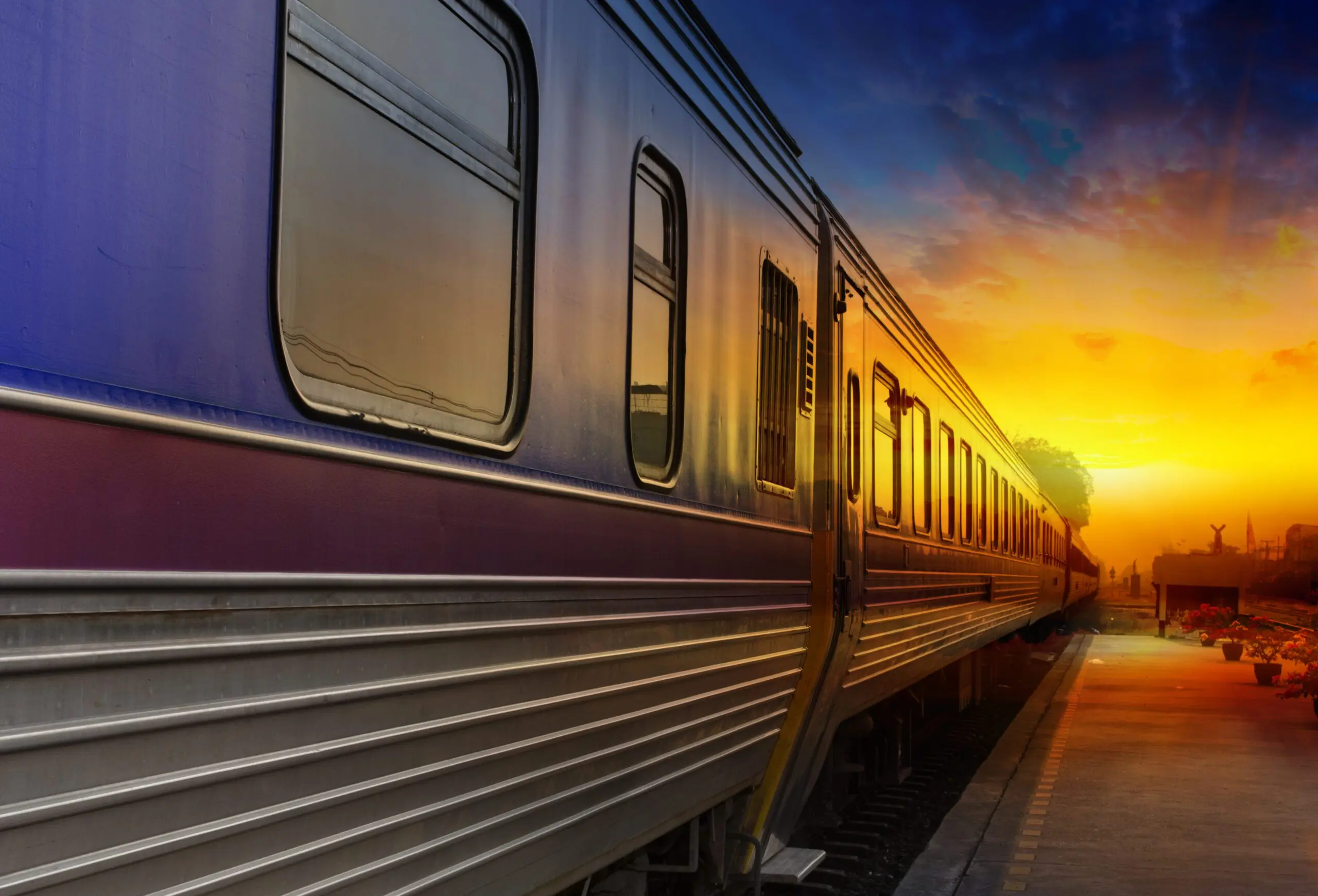 Train sits at a platform with windows reflecting a bright sunset sky and long shadows.