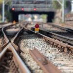Multiple railway tracks split and merge with a signal, leading toward a bridge in the background.
