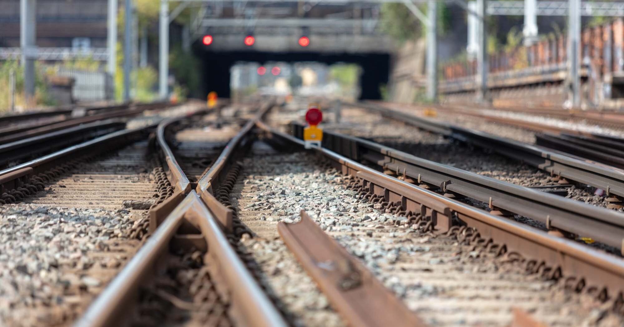 Multiple railway tracks split and merge with a signal, leading toward a bridge in the background.