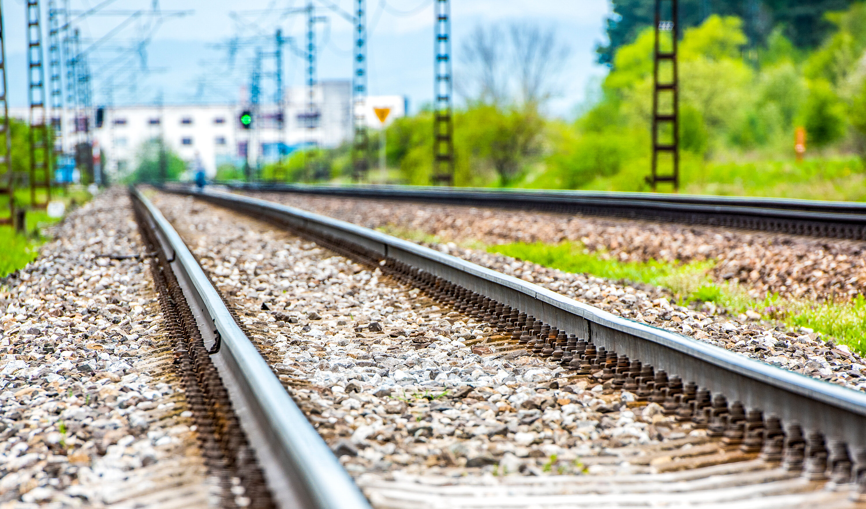 Two parallel railway tracks on gravel ballast with overhead lines and greenery along the side.