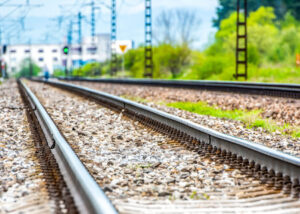 Two parallel railway tracks on gravel ballast with overhead lines and greenery along the side.