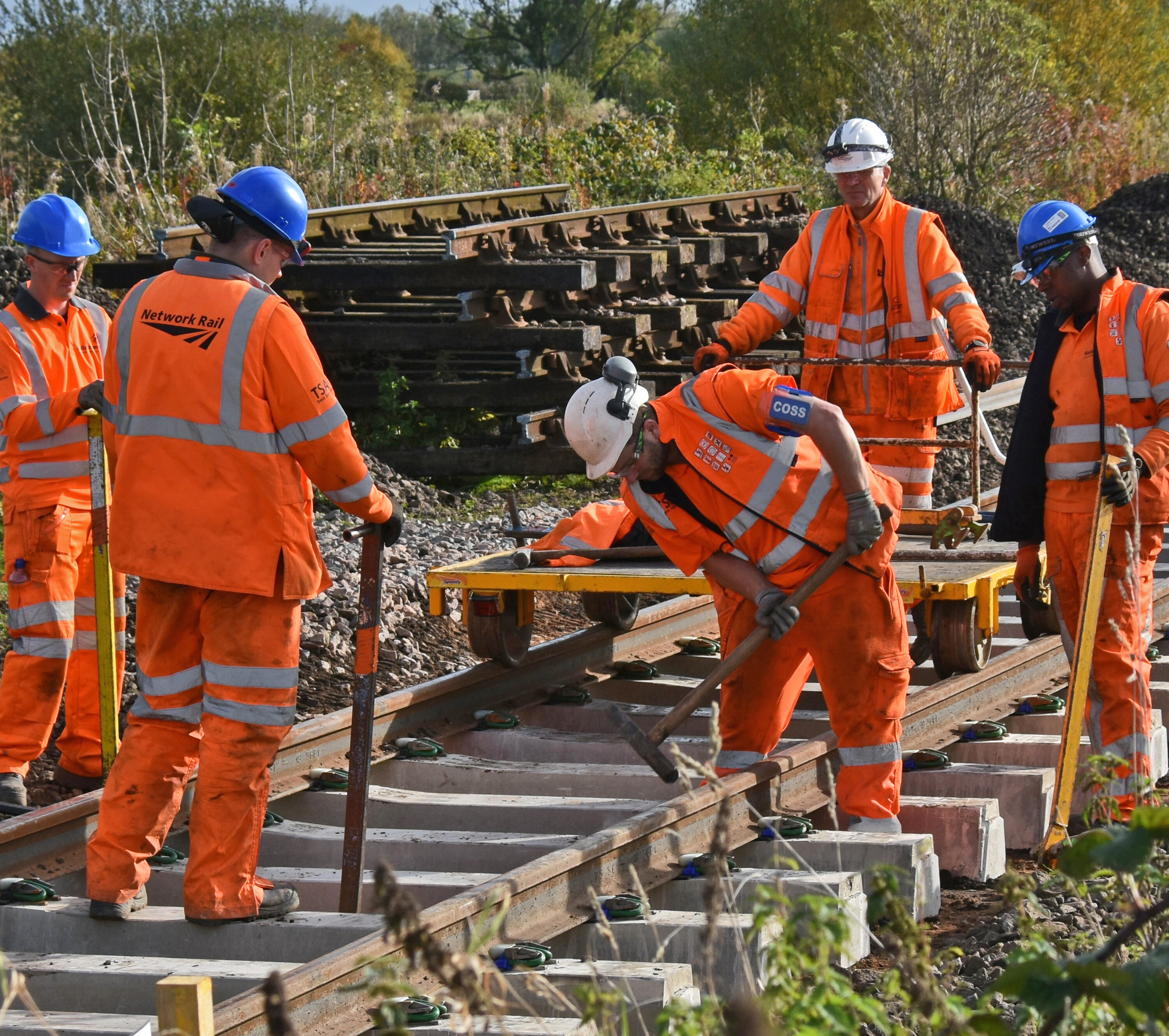 Five workers in high-visibility clothing install and secure new railway track components outdoors.