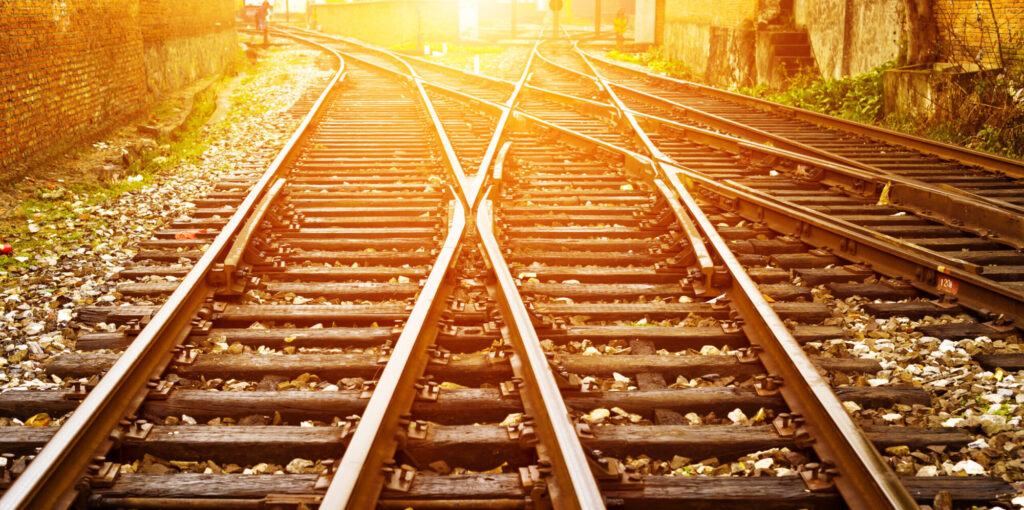 Multiple railway tracks split and cross at a junction, lit by warm sunlight between brick walls.